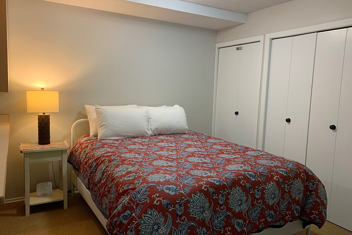 Queen bedroom with red bedding, bedside table, and lamp