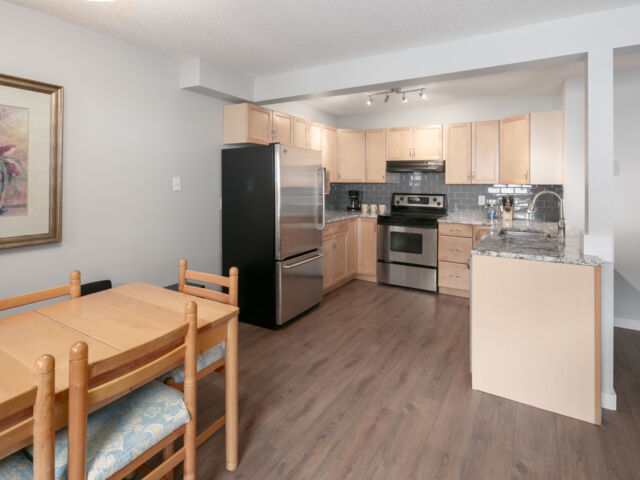 Kitchen and dining area with light wood dining table to the left, stainless steel appliances, and counterspace.