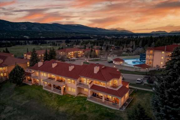 Tee House 3BR-13 exterior at night with illuminated balconies, nearby pool and mountain views in Fairmont Hot Springs
