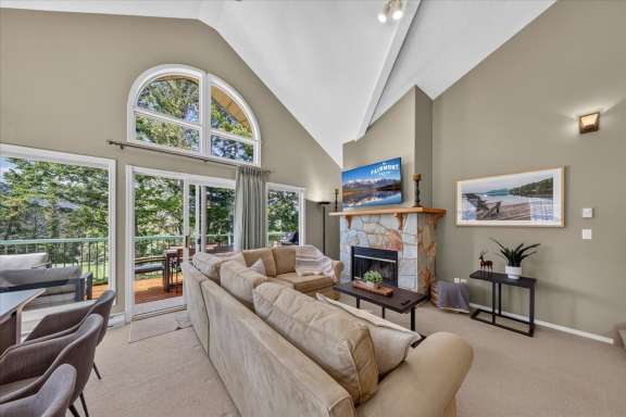 Bright open-concept living room with soaring vaulted ceilings, a wood fireplace, Smart TV, comfortable seating, and large windows with access to the wrap-around deck at Springs & Swings - Marble Canyon 504 - Phase 1