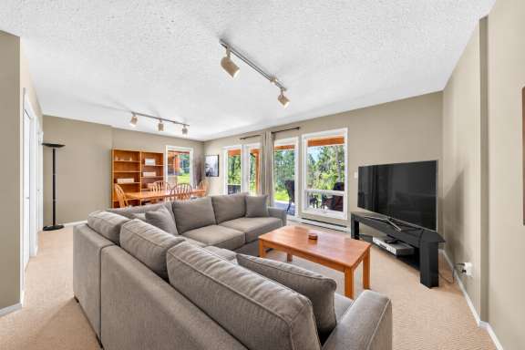 Lower living room at Springs & Swings – Marble Canyon 504 with grey sectional sofas, TV, dining area and large windows overlooking the golf course