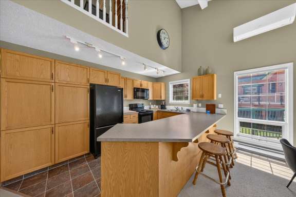 Fully equipped open-concept kitchen featuring a large breakfast bar with seating for 3, stovetop, oven, microwave, dishwasher, full-size refrigerator and ample counter space in Springs & Swings - Marble Canyon 504 - Phase 1.
