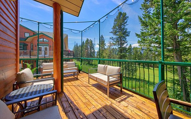 Open-concept living room with vaulted ceilings, a stone fireplace, large sectional sofa, dining area, and expansive windows overlooking the surrounding trees and deck in a Fairmont Creek vacation rental