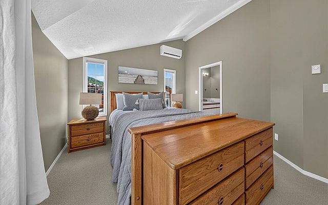 Open-concept living room with vaulted ceilings, a stone fireplace, large sectional sofa, dining area, and expansive windows overlooking the surrounding trees and deck in a Fairmont Creek vacation rental