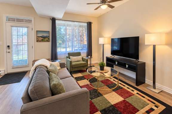 Bright living room at Little Falls Landing with a sofa, armchair, large TV, coffee table and large window overlooking the outdoor patio area