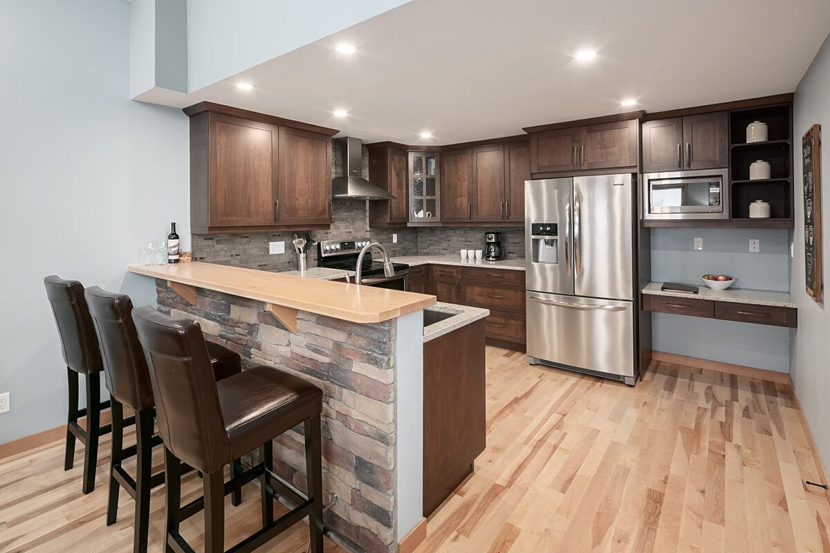 Kitchen area with three barstools, island, and stainless steel appliances.