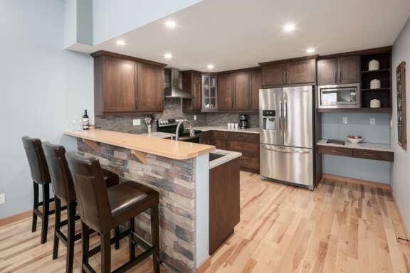 Kitchen area with three barstools, island, and stainless steel appliances.