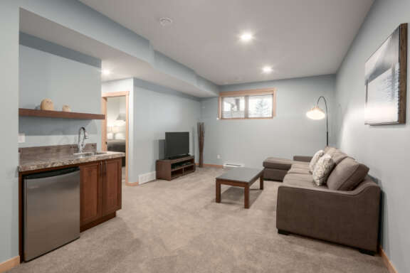 Living space in a downstairs area. Television, couch, coffee table and wet bar.