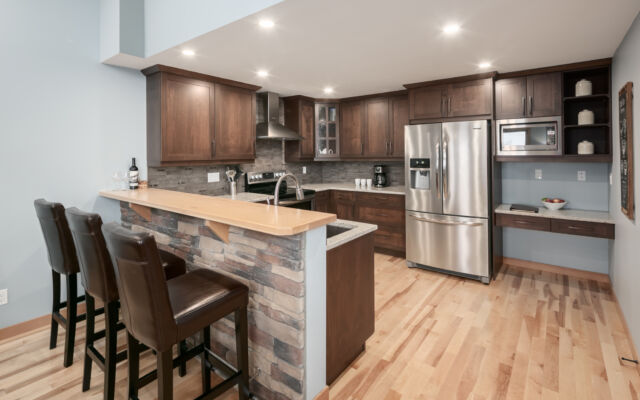 Large living room with windows to the right. Television above, two couches, one chair and coffee table.