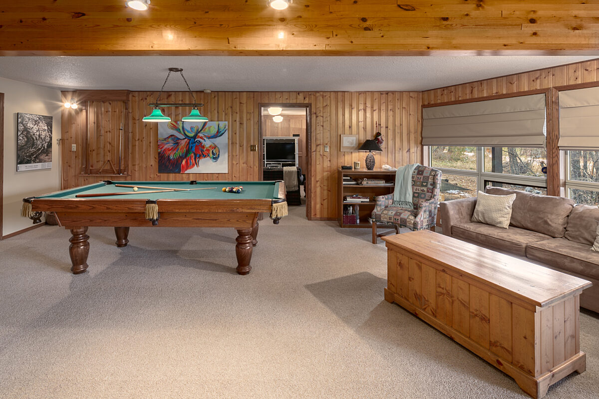 Recreation room with pool table, bar area, couch, windows to the right, and seating.