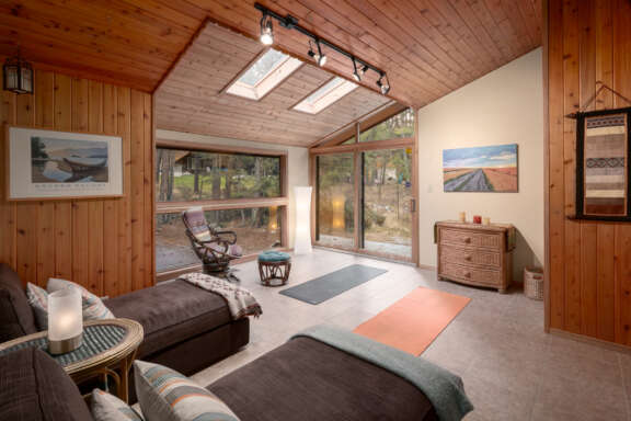 Bedroom 2 with daybeds that convert to queen beds. Wood panelling on the walls, large window to the left, and two yoga mats on the floor to the right.