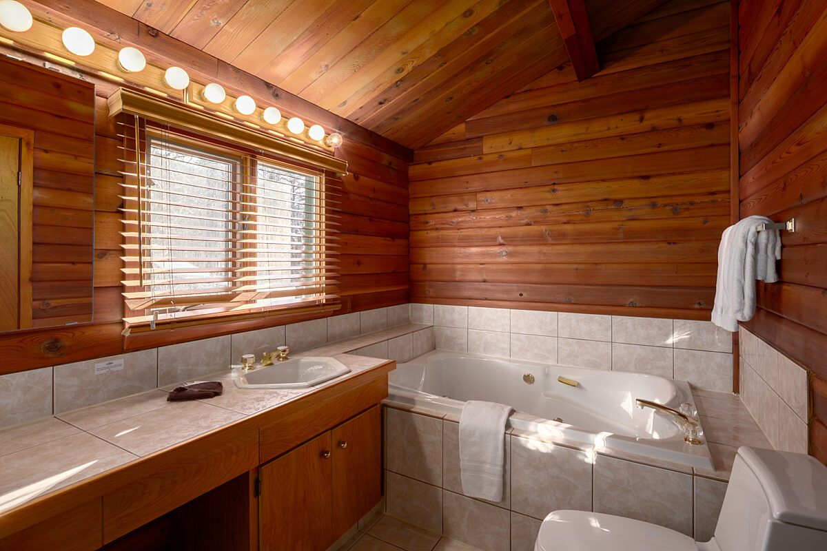 Rustic bathroom with bathtub and sink. Mirror with lights above sink. Wood panelling on the walls.