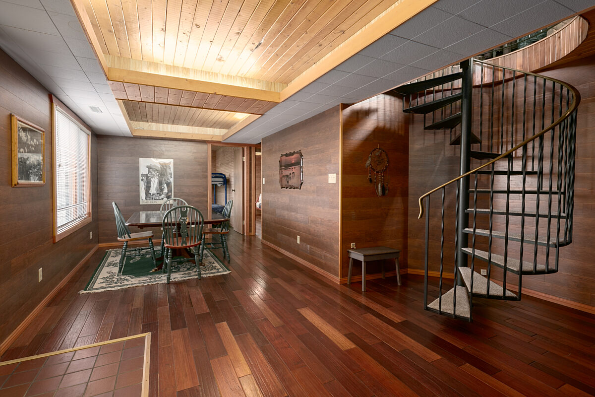 Lower level of a home with a spiral staircase leading to dark wood panelled walls and bedrooms.