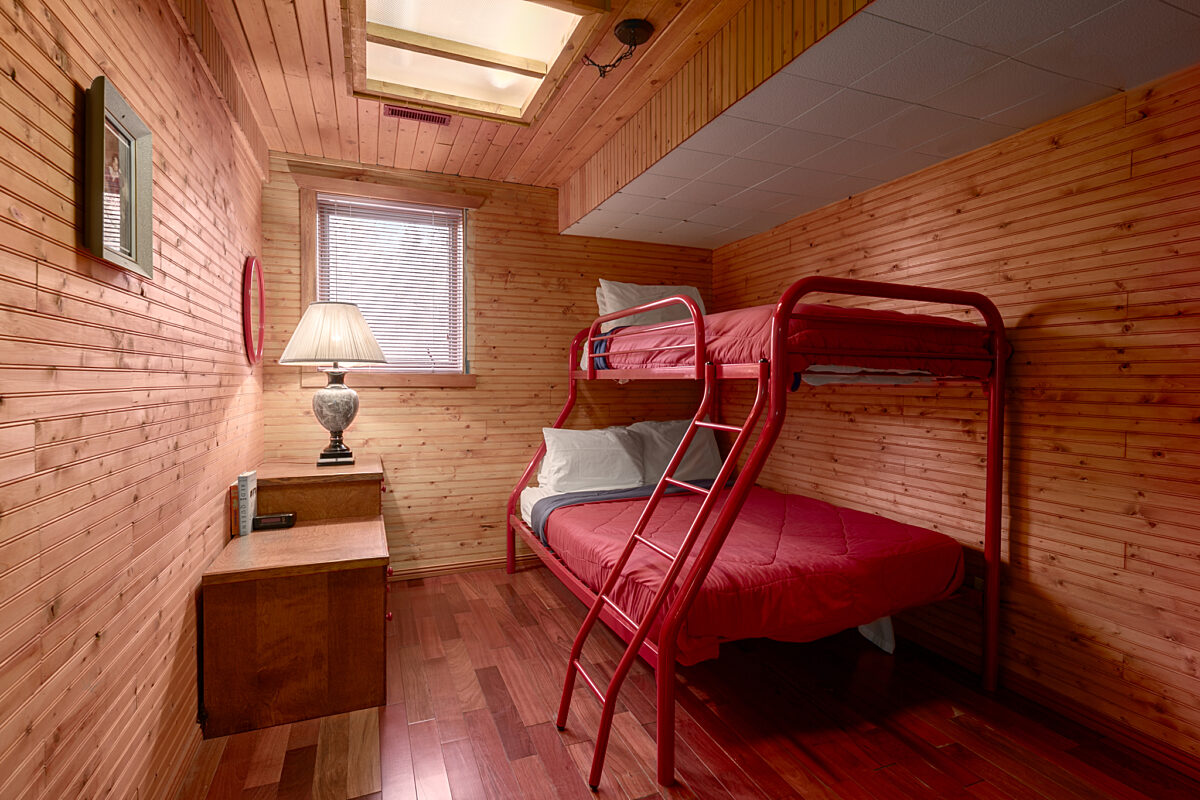 Wood panelled bedroom. Bunk bed with queen on the bottom half and twin on the top. Red bedding.