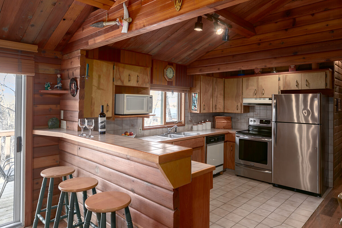 Kitchen area with wooden interior, island with barstools, and stainless steel appliances.