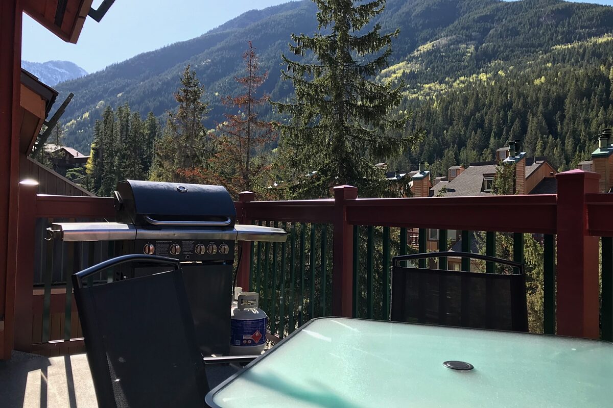 Outdoor patio with views of mountains, trees, and other accommodations. Barbecue on deck, patio furniture, table, and chairs.