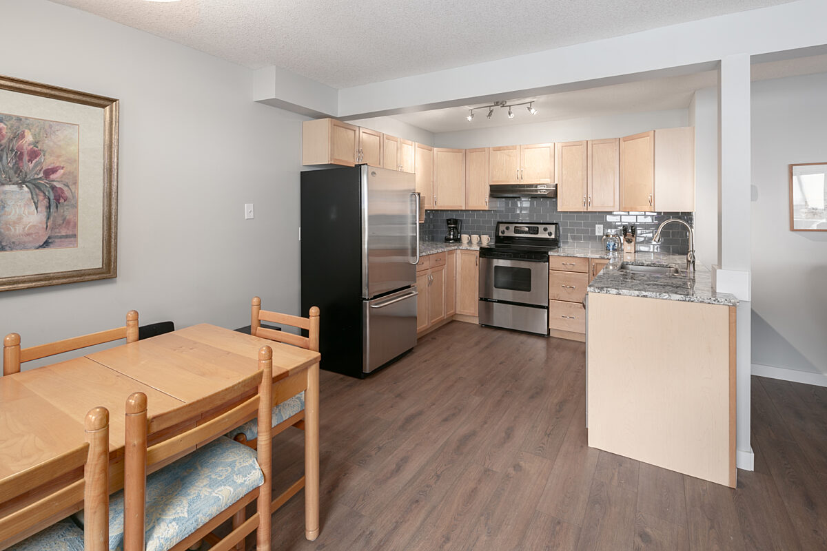 Kitchen and dining area with light wood dining table to the left, stainless steel appliances, and counterspace.