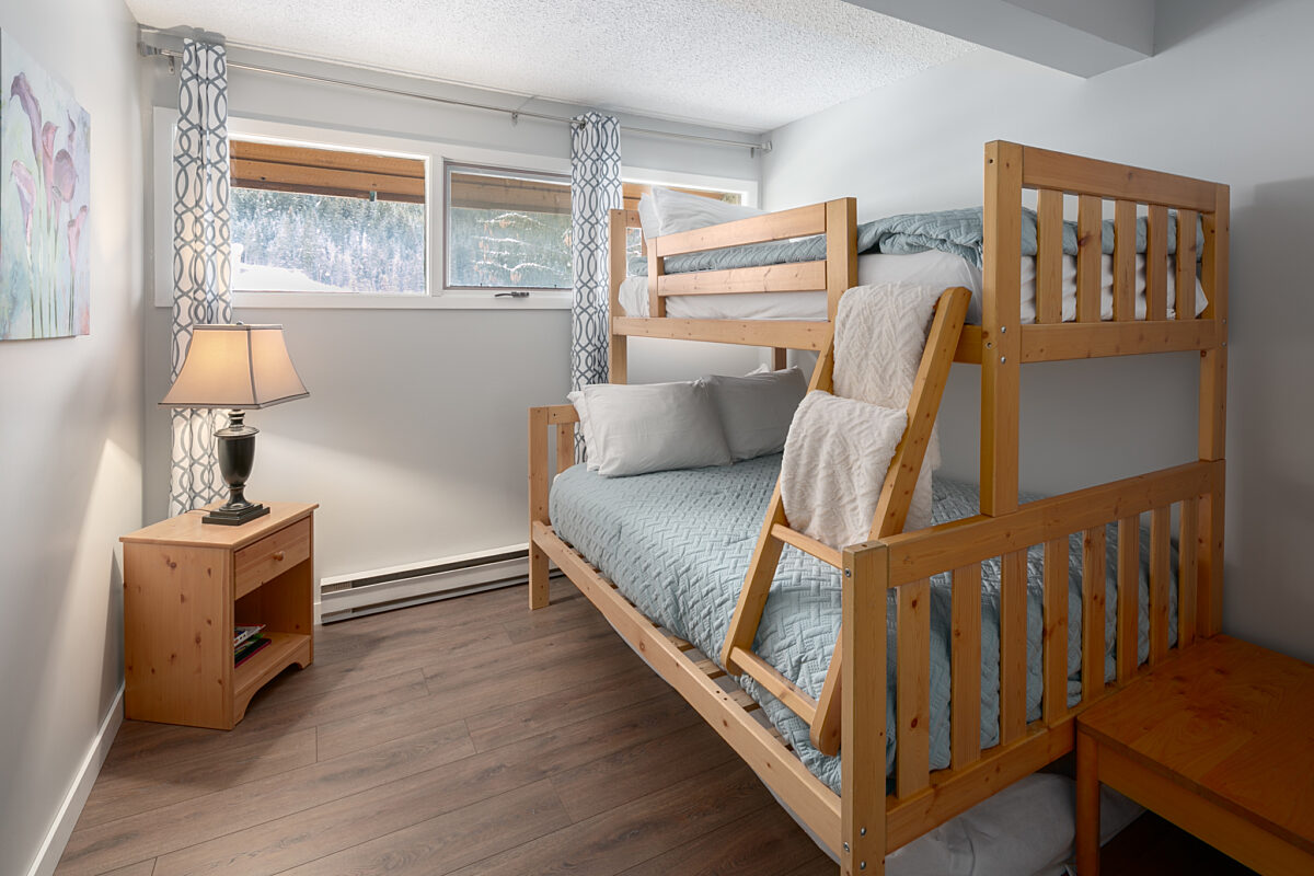 Twin over double bunk bed with night table and lamp to the left.