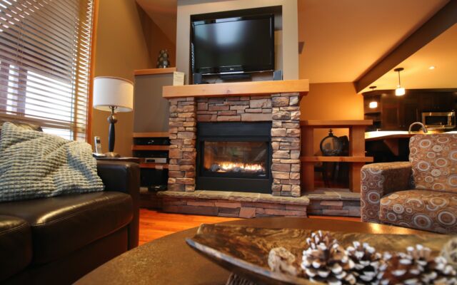 Living room area with couches, windows to the left, stone fireplace and television.
