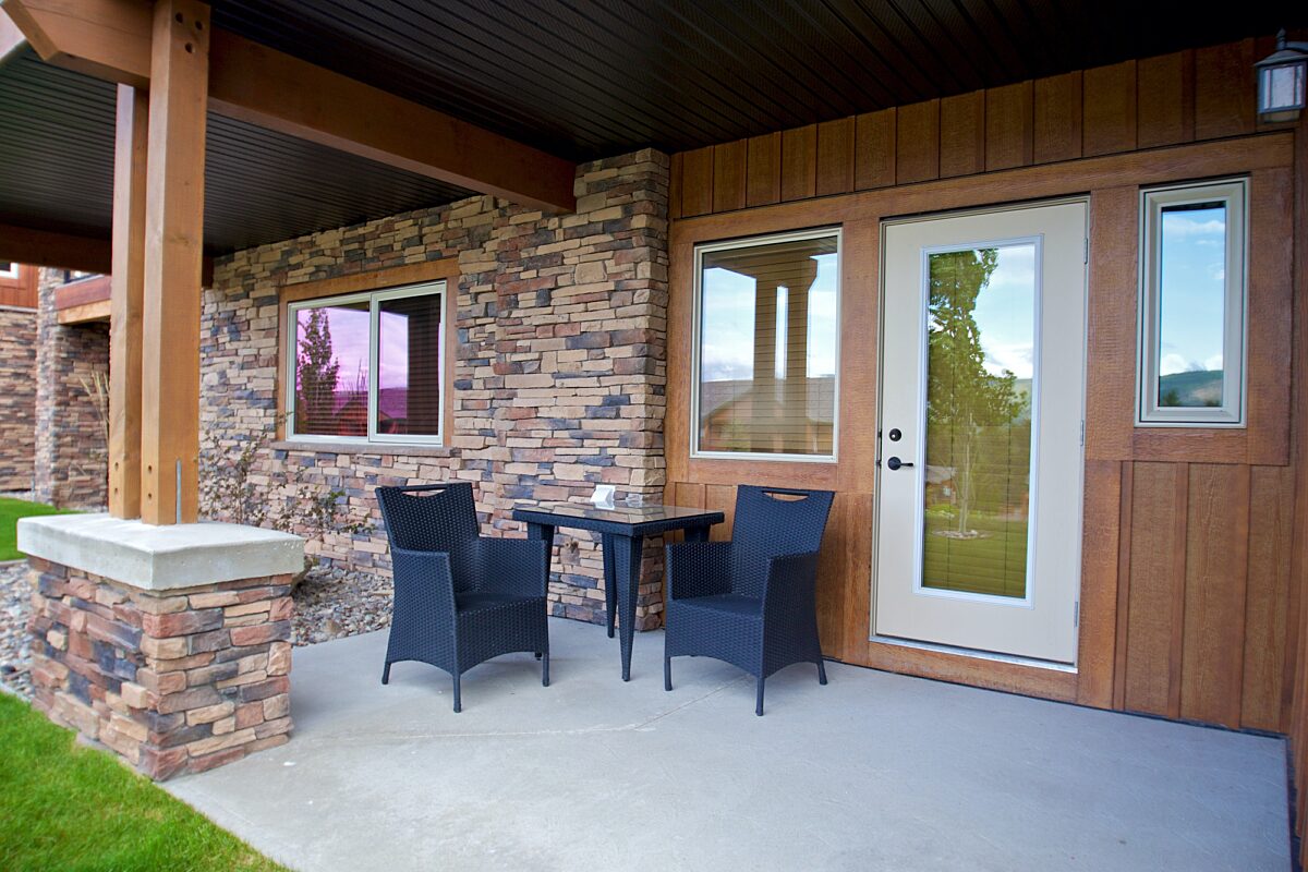 Patio with two black chairs and coffee table. White door leads to the interior. Brick exterior of house.