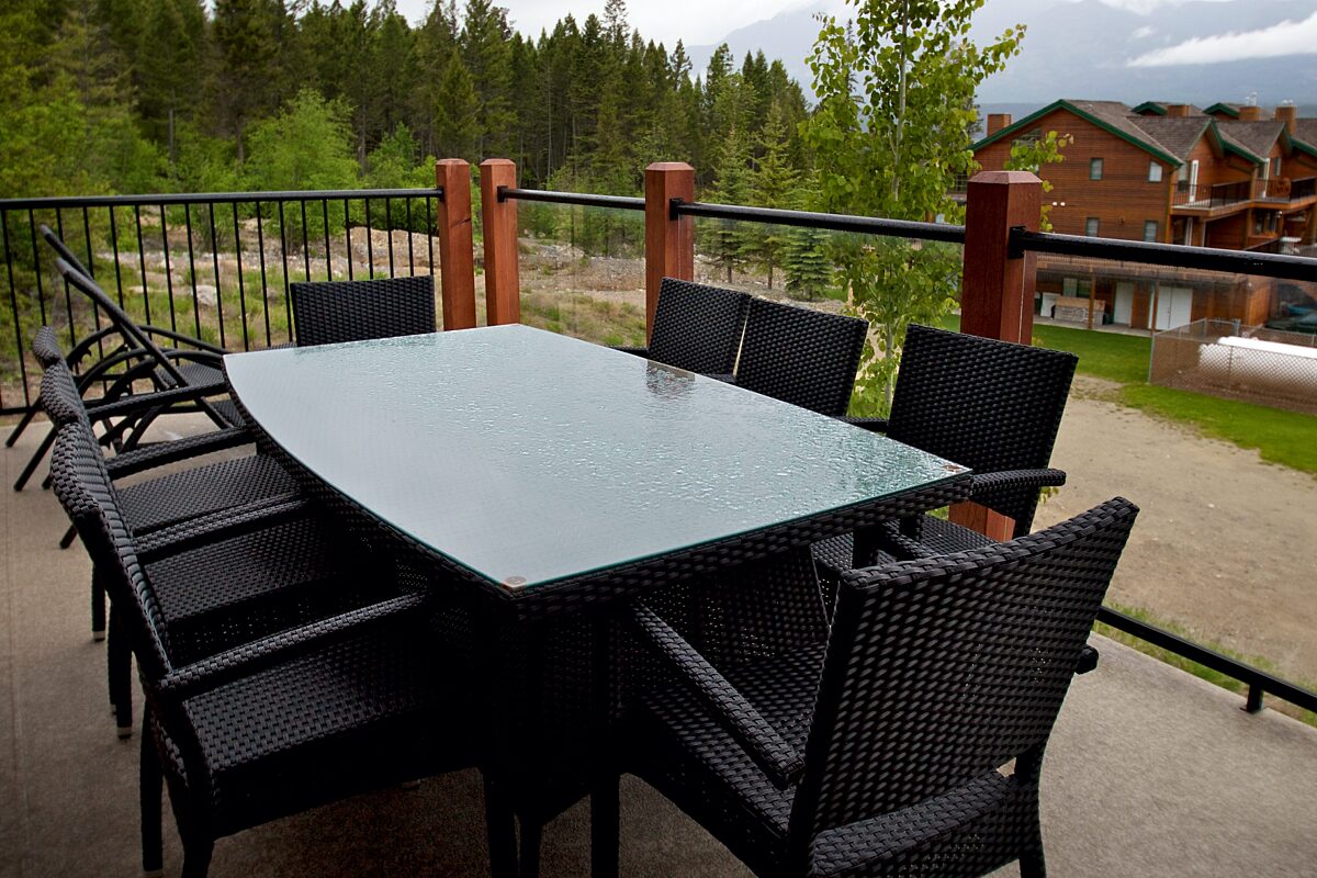 Large black table with chairs on outdoor patio. Trees and other properties in view.