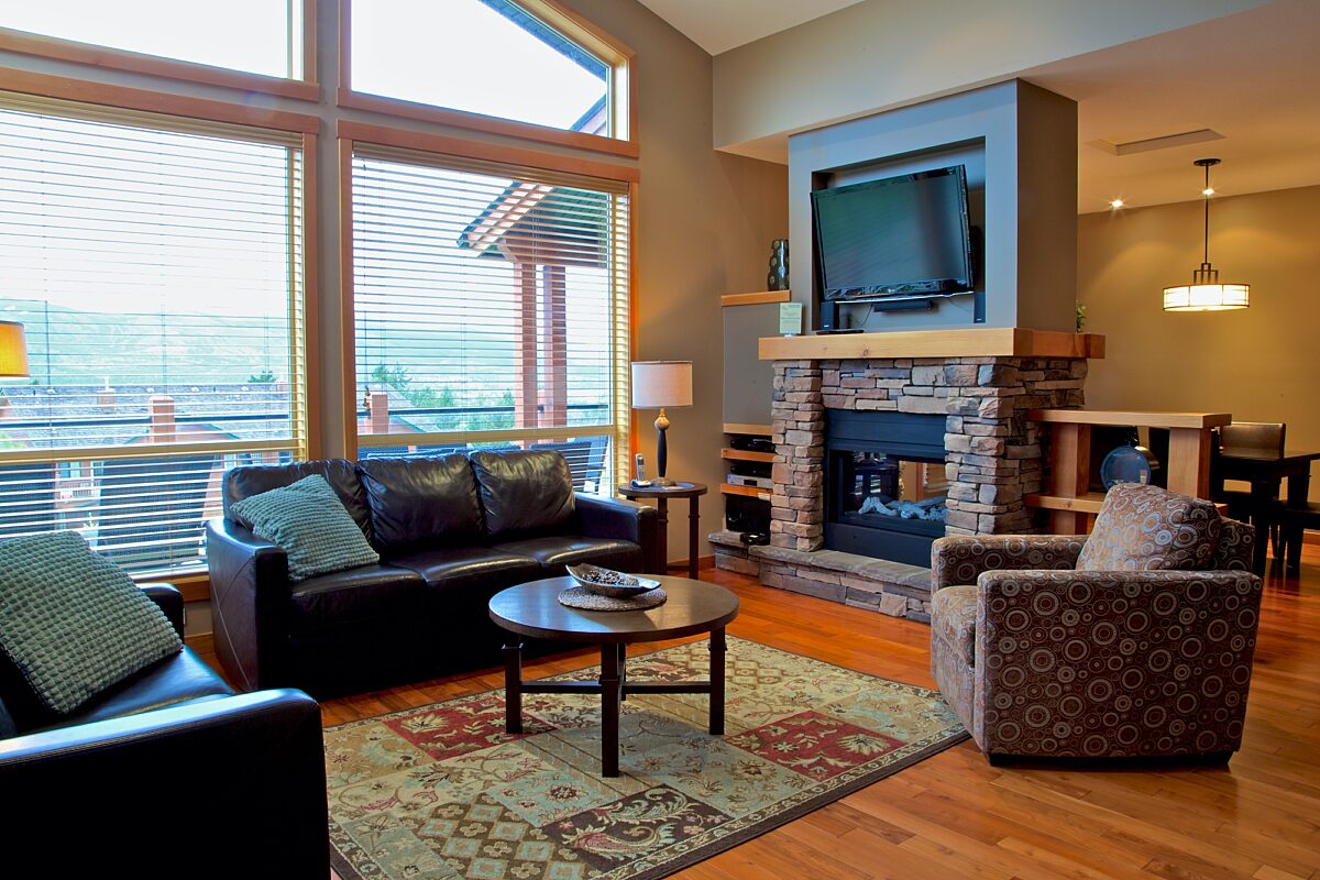 Living room area with couches, windows to the left, stone fireplace and television.