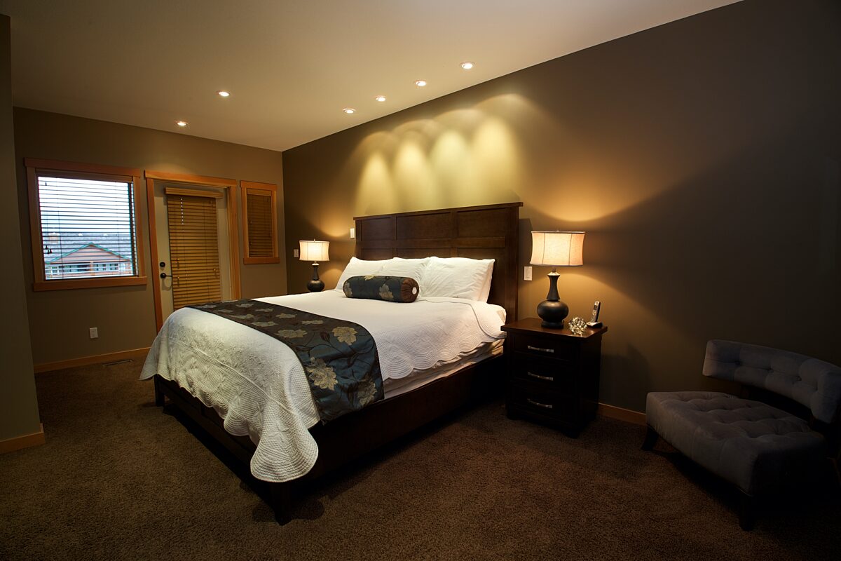 Master bedroom with king bed. Two night tables with lamps and strip of lighting overhead.