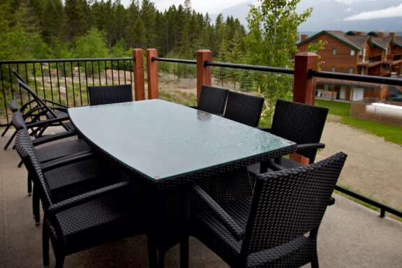 Large black table with chairs on outdoor patio. Trees and other properties in view.