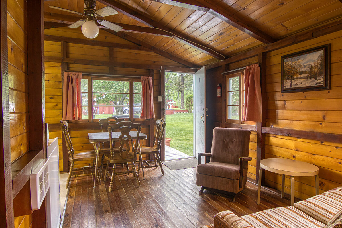 Dining area with wood panelling. Table with four chairs to the right, rocking chair to the left with coffee table.