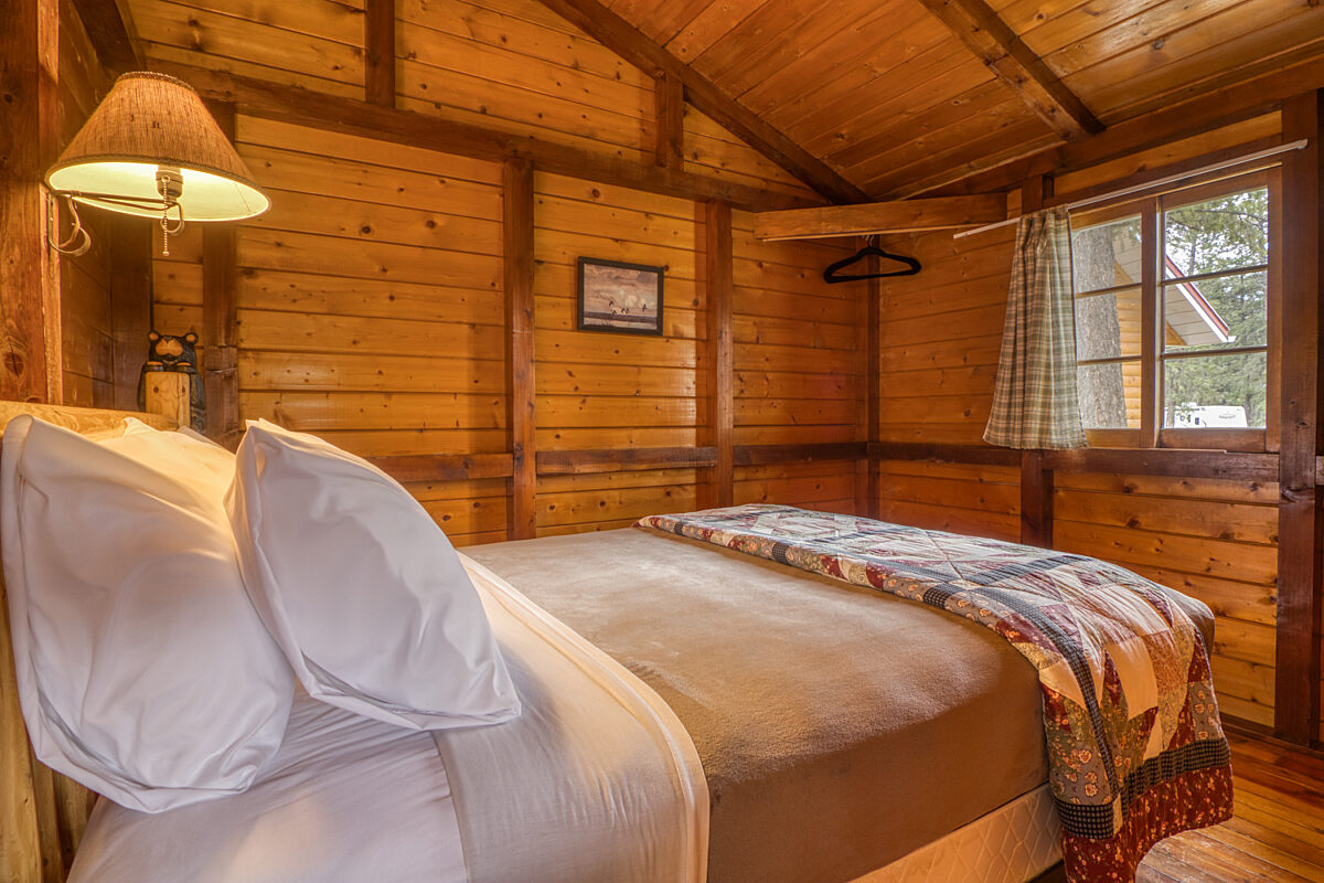 Queen bedroom in wood panelled cabin. Lamp and blanket.