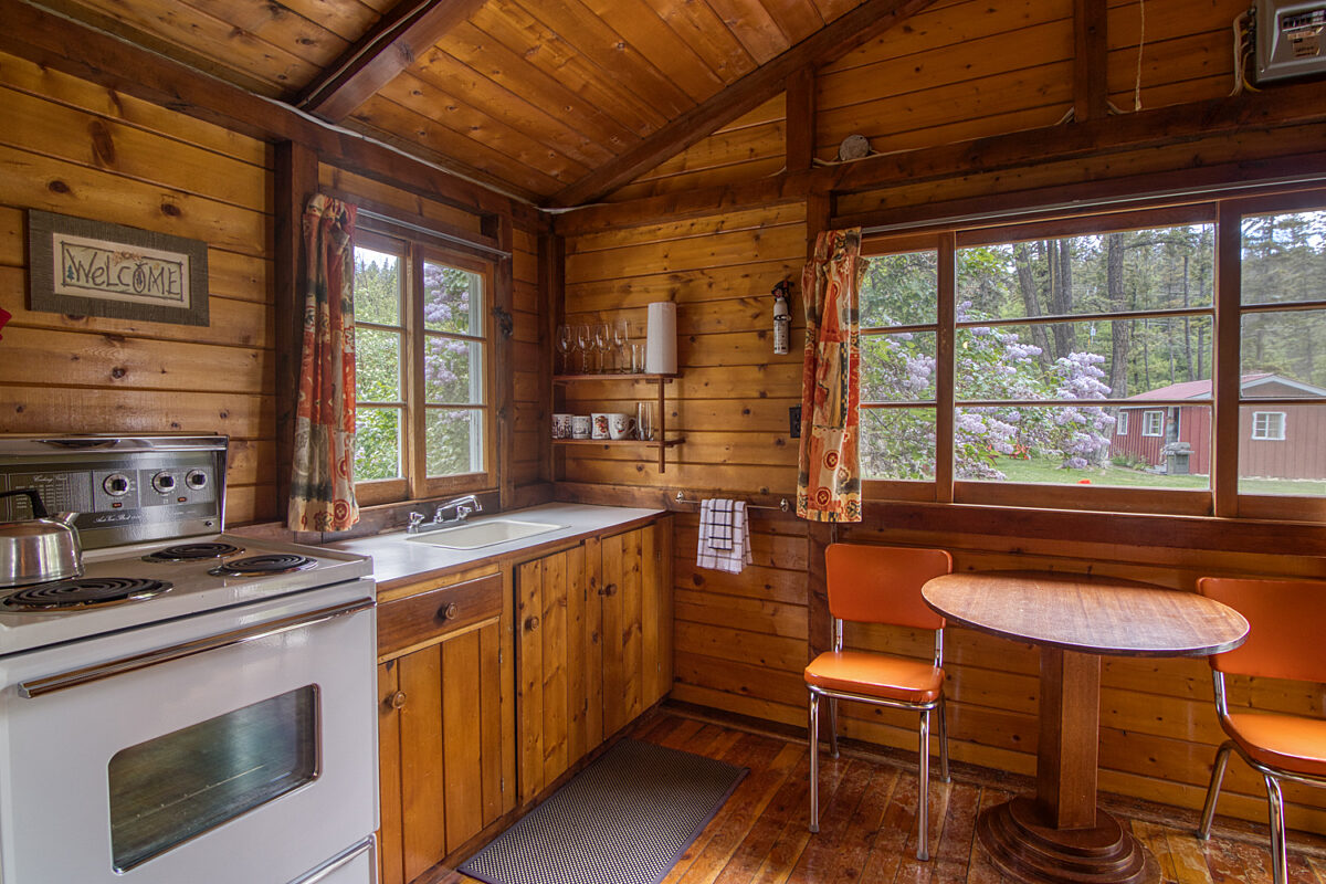 Wood panelled kitchen area with small dining table, two chairs, and oven to the right.