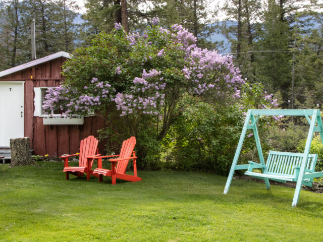 Outdoor living space with two red chairs and teal swing.