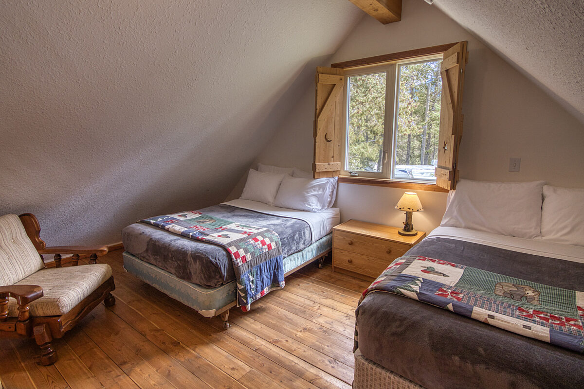 Loft with two double beds. Window between the two beds with bedside table and lamp.