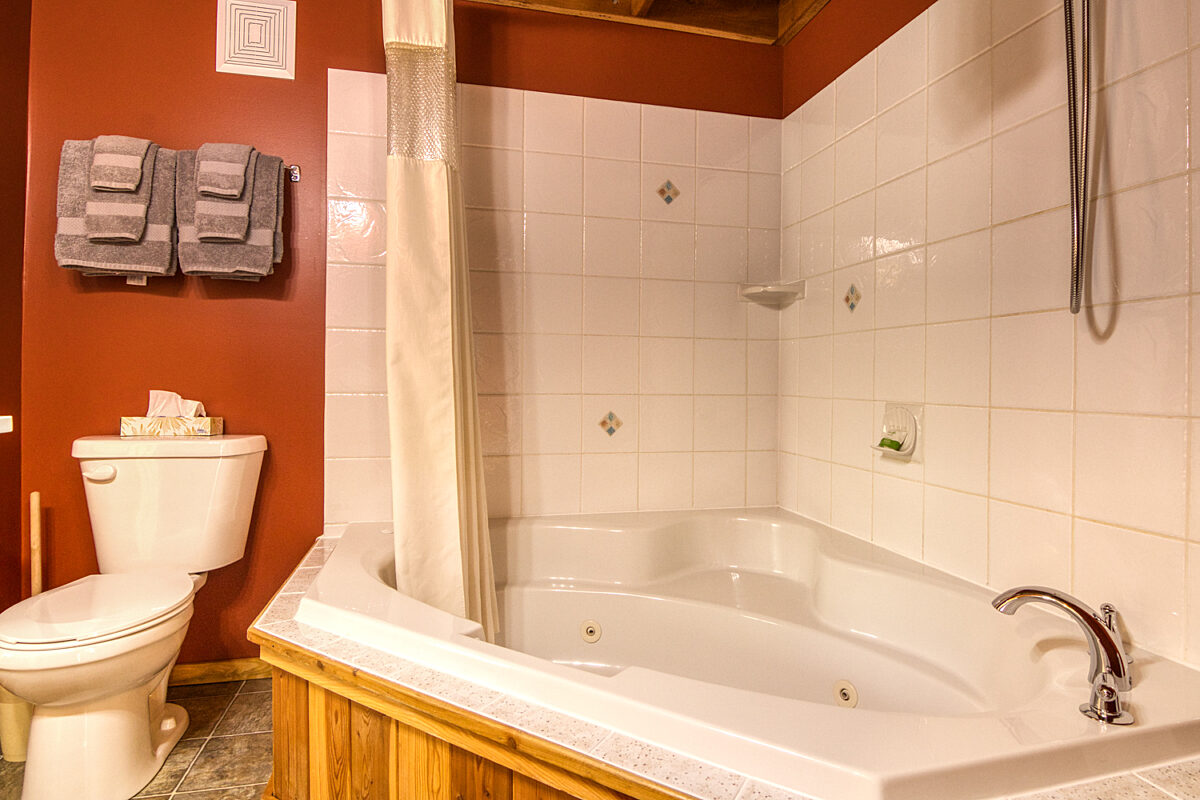 Bathroom with white tilled bathtub and shower, toilet, and red walls.