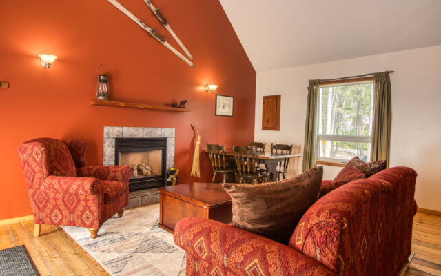 Wood cabin with red roof and white doors. BBQ on the patio and red chairs outside. Green grass outside.