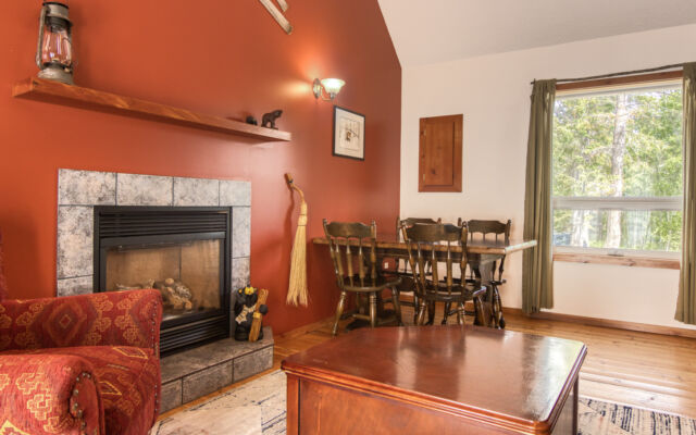 Wood cabin with red roof and white doors. BBQ on the patio and red chairs outside. Green grass outside.