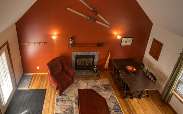 Wood cabin with red roof and white doors. BBQ on the patio and red chairs outside. Green grass outside.