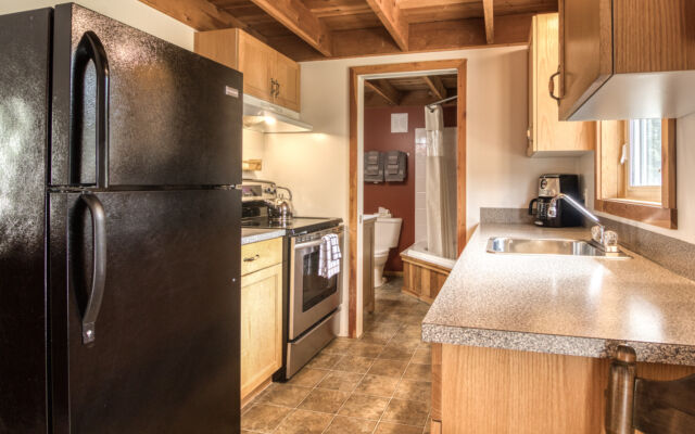 Wood cabin with red roof and white doors. BBQ on the patio and red chairs outside. Green grass outside.