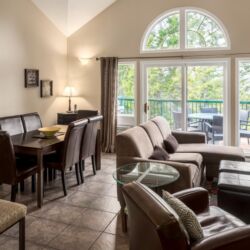 Living area with dining room table, couch, chairs, a large window with curtains.