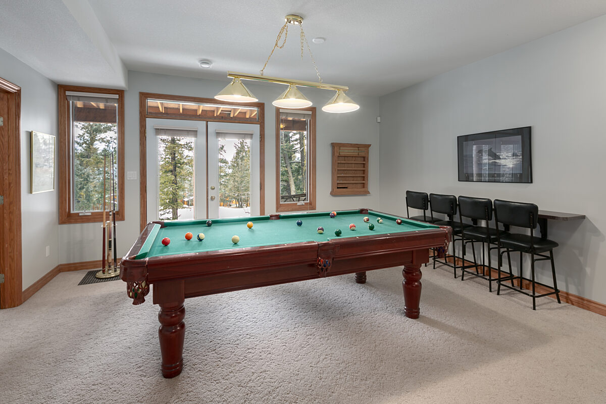 Room with pool table, barstools, and windows.