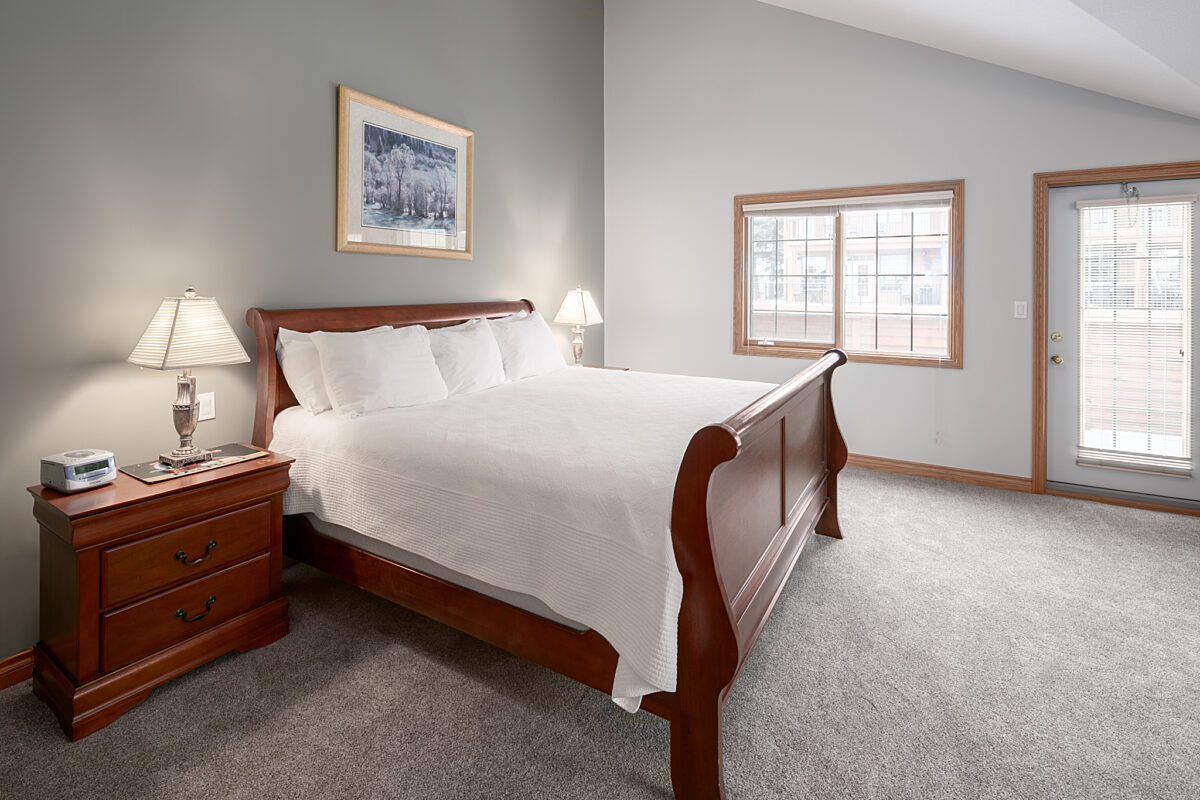King bedroom with white bedding, bedside tables with lamp, and white walls