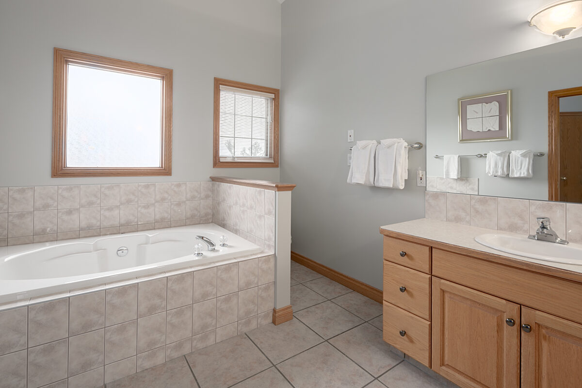 Ensuite bathroom with bathtub, vanity, mirror, and sink.