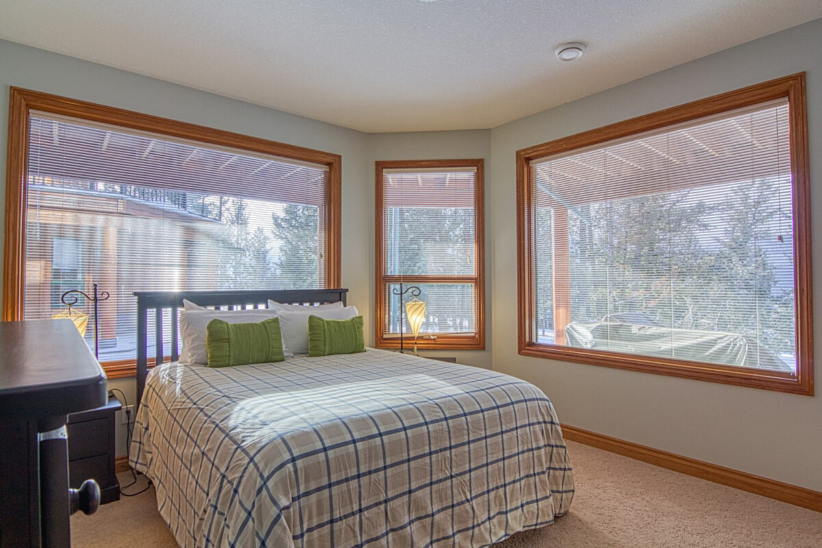 Queen bedroom with queen bed, three windows, and green decorative pillows.