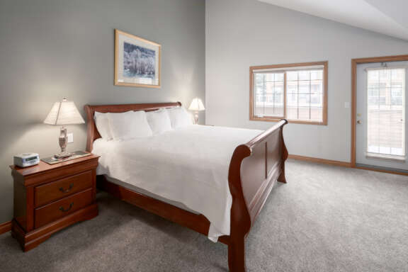 King bedroom with white bedding, bedside tables with lamp, and white walls