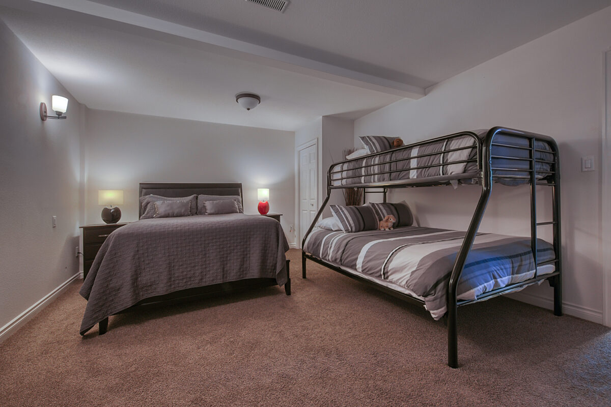 Bedroom with double bed and bunk bed. Grey bedding and two bedside tables with lamps.