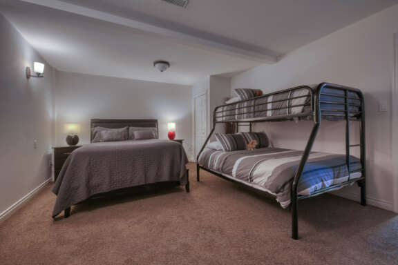 Bedroom with double bed and bunk bed. Grey bedding and two bedside tables with lamps.