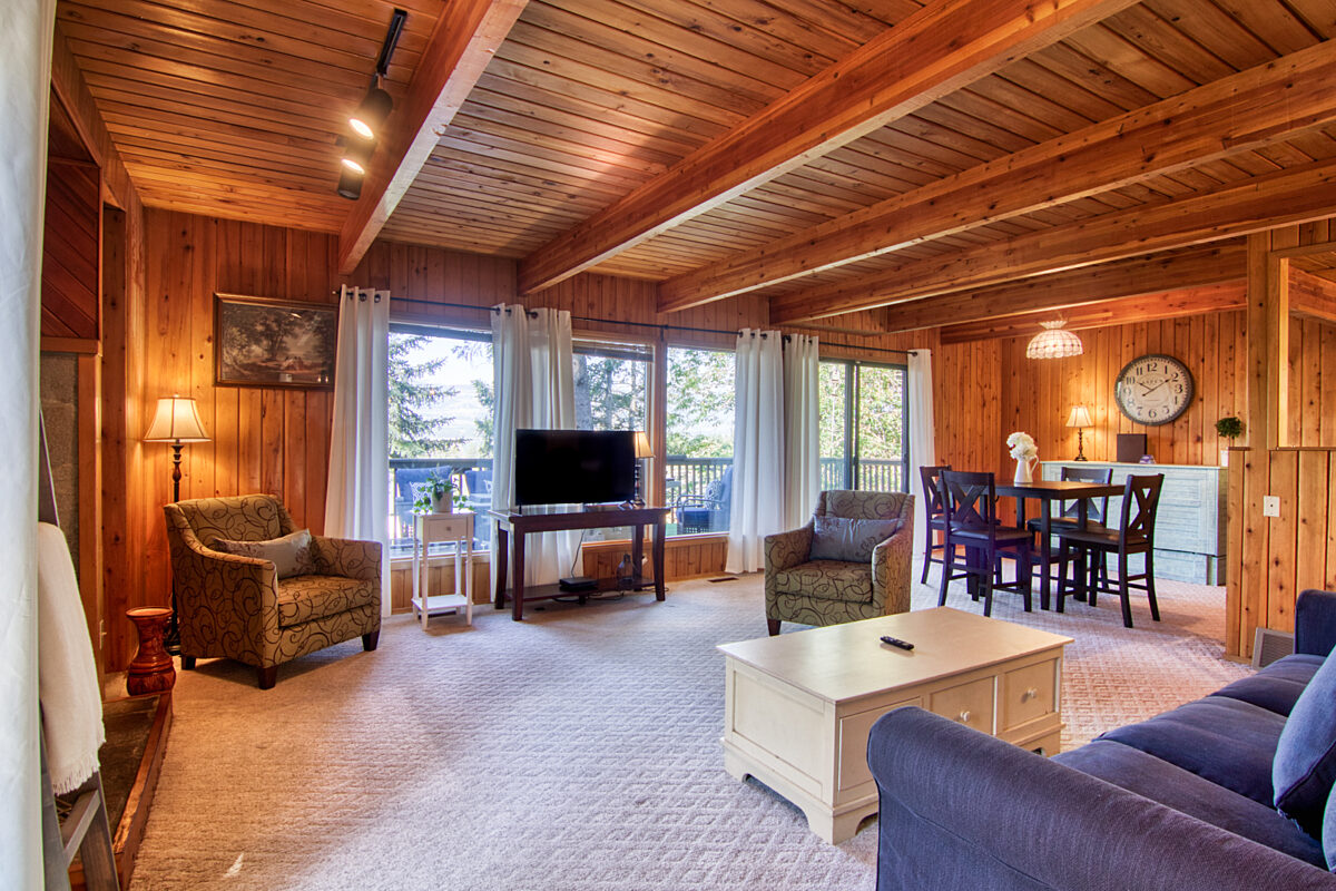Living area with wood panelling throughout the room, a couch, coffee table, and chairs. Dining area in background.