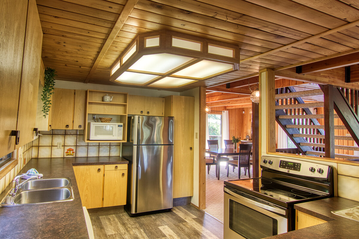 Retro kitchen with appliances, cupboards, and sink. Stairs and dining area in the background.