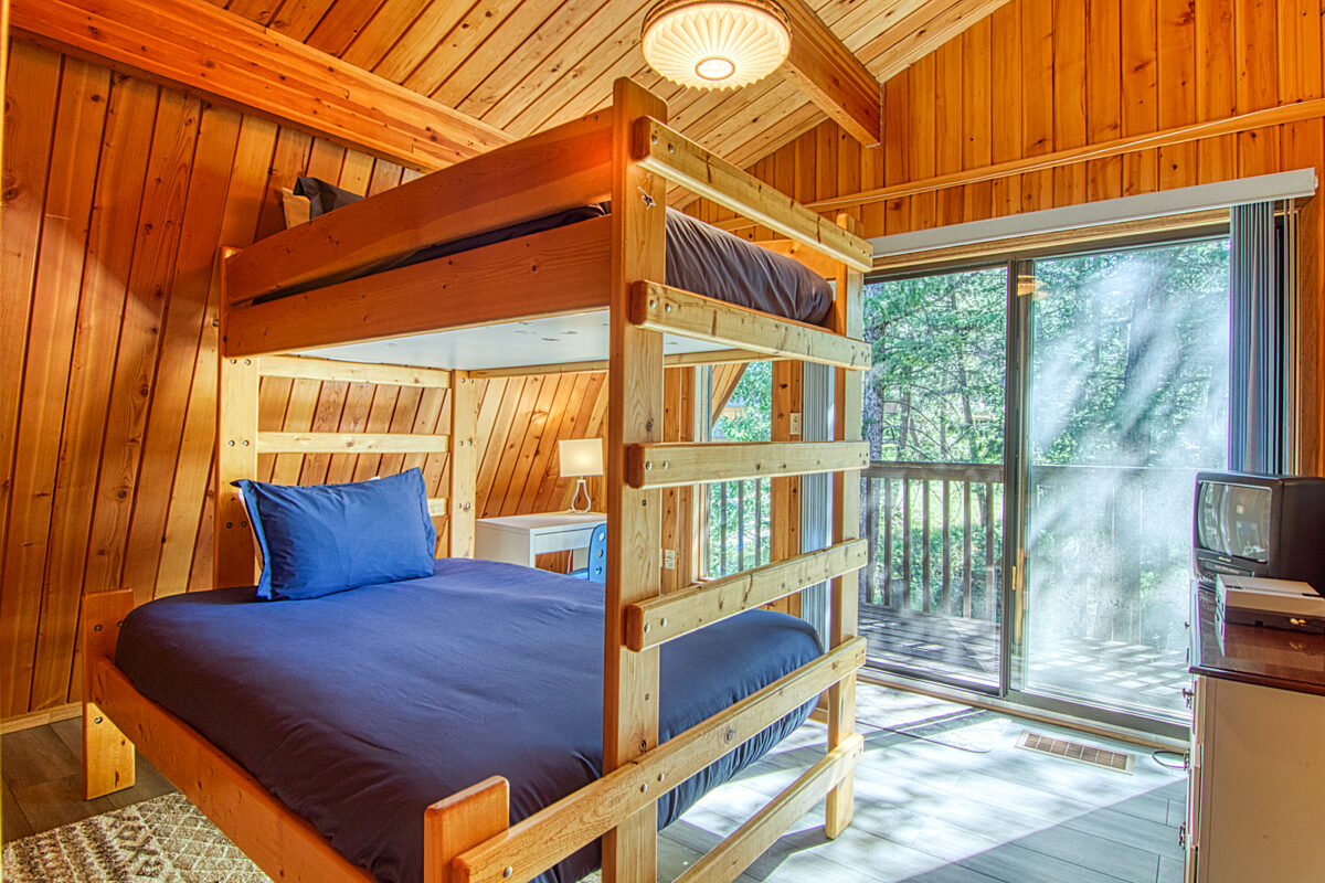 Bed beds with blue bedding in wood panelled room. Large window to the right.