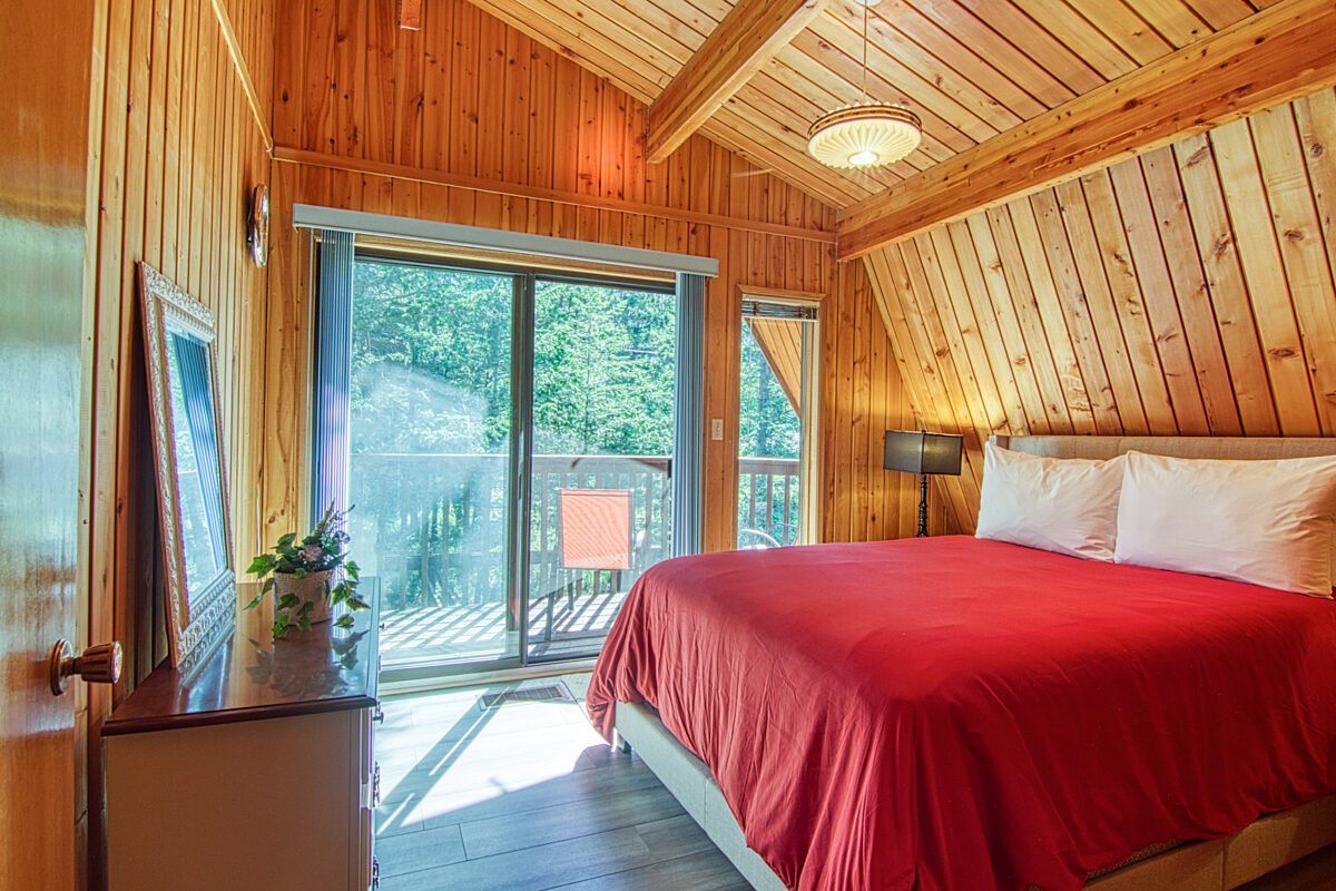Bedroom with queen bed with red bedding. Wood panels on the walls and doors to patio.